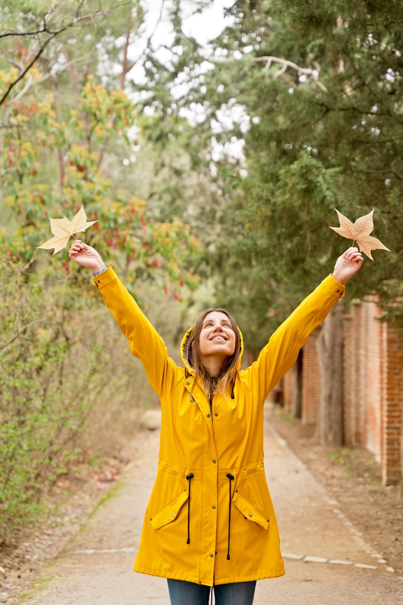 Front view of happy woman raising arms with maple leaves